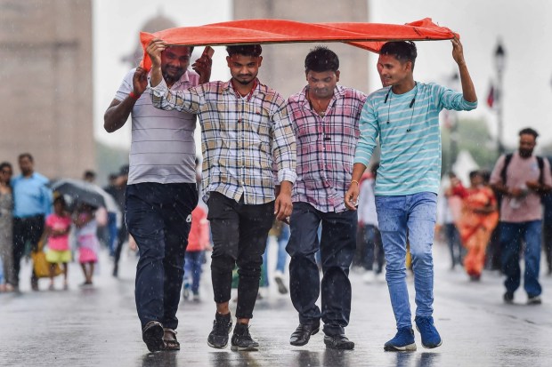People covering themselves to protect from rain walk on a road, near India Gate in New Delhi. (Image: PTI)