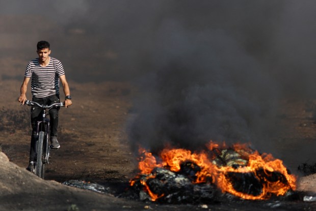 A Palestinian rides a bicycle next to a fire during a protest against Israeli army raid in Jenin on July 3, 2023. (Image: Reuters)