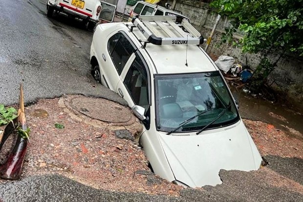 A car falls into a crater formed after a road caved in due to heavy monsoon rains, in Lucknow. (Image: PTI Photo)