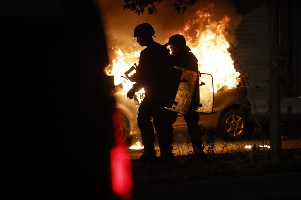 Riot police stand near a burning car in the La Meinau neighborhood of Strasbourg, eastern France, on Friday, June 30, 2023. Young rioters clashed with police and looted stores on the fourth day of violence triggered by the deadly police shooting of a teen, piling more pressure on President Emmanuel Macron after he appealed to parents to keep children off the streets and blamed social media for fueling unrest. (Image: AP/PTI)