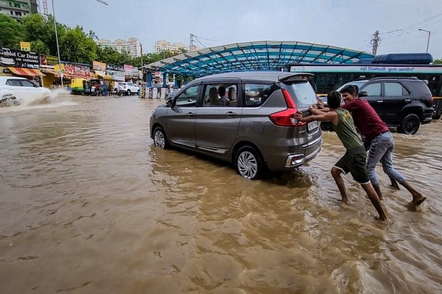 Locals help move a car stuck on a waterlogged road at Subhash Chowk after monsoon rain, in Gurugram on July 9, 2023. (Image: PTI Photo)