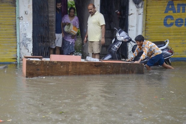 Residents use a wooden slab to prevent rainwater from entering their house during monsoon rain, in Gurugram on July 9, 2023. (Image: PTI Photo)