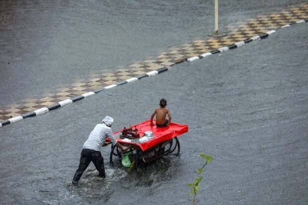 A vendor pushing his cart wades through a waterlogged road amid heavy monsoon rains, near Inderlok Metro Station in New Delhi. (Image: PTI Photo)