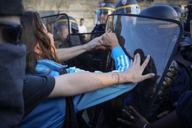 Police officers face protesters on Concorde square during a protest in Paris, France. French President Emmanuel Macron urged parents Friday to keep teenagers at home and proposed restrictions on social media to quell rioting spreading across France. (Image: AP Photo/Lewis Joly)