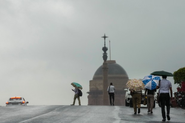 People holding umbrellas walk to their offices in New Delhi. (Image: PTI)