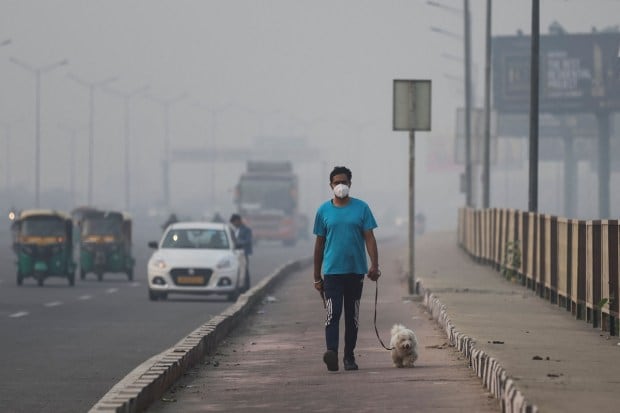 A man wearing face mask walks with his dog on a footpath amidst the morning smog in New Delhi on Tuesday. (Reuters)