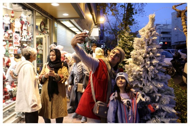 An Iranian woman captures a festive moment, taking a selfie with her child in front of a Christmas store in Tehran, Iran, on December 25, 2023. (Image: WANA via REUTERS)