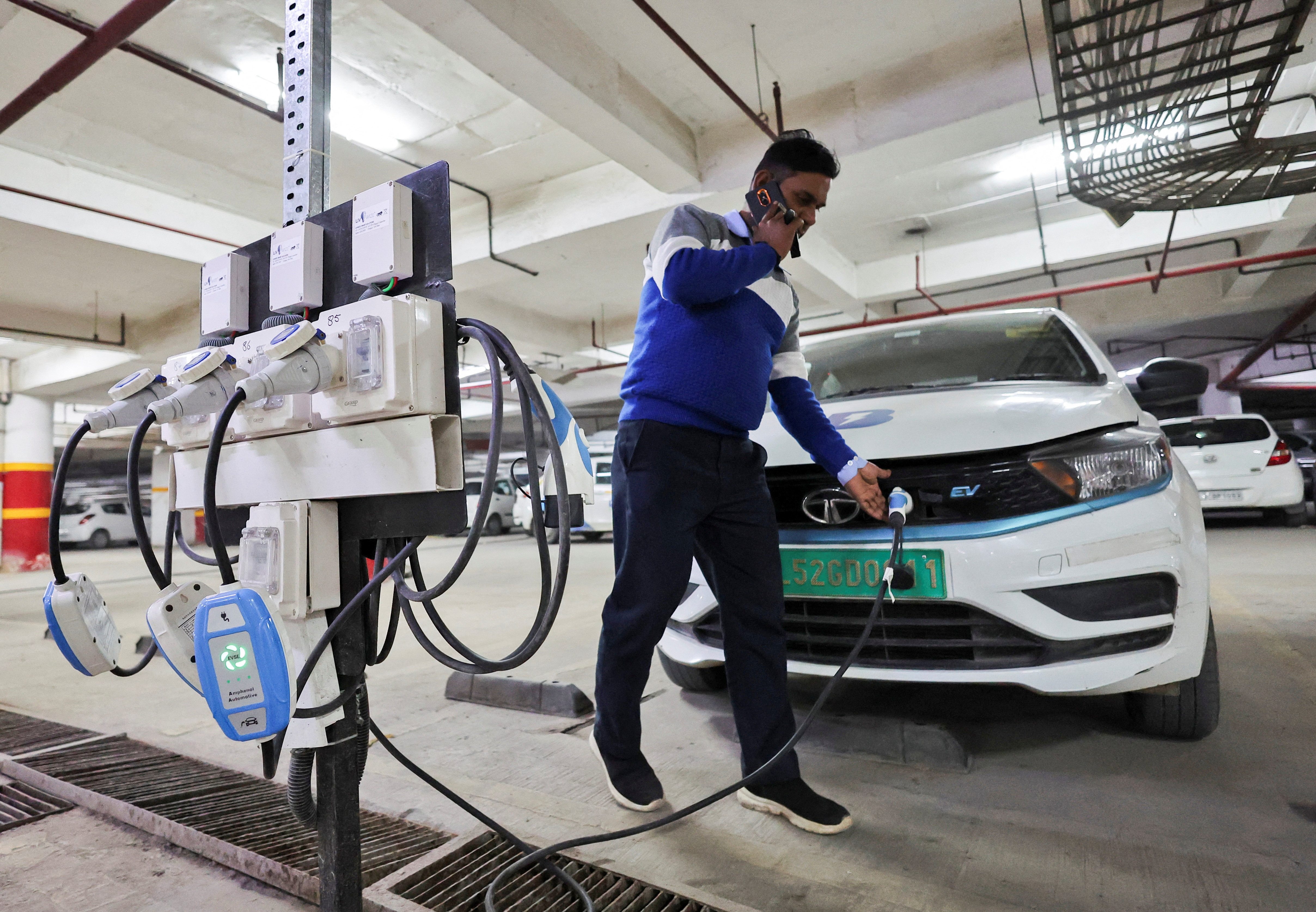 A man charges an electric vehicle (EV) at the charging hub of Indian ride-hailing BluSmart Electric Mobility in Gurugram (Image/Reuters)