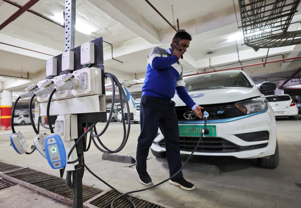 A man charges an electric vehicle (EV) at the charging hub of Indian ride-hailing BluSmart Electric Mobility in Gurugram (Image/Reuters)