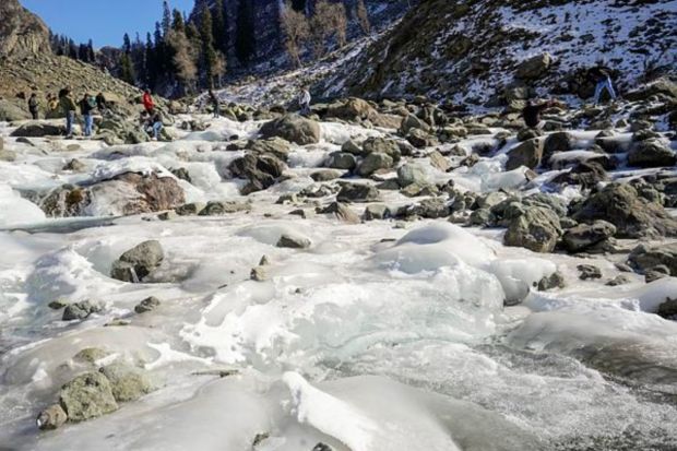 Tourists at a frozen stream, at Chandanwari in Anantnag district, Sunday. Several parts of Kashmir recorded minimum temperature below the freezing point as 'Chilla-i-Kalan', a 40-day period of harsh winter, grips the valley. (PTI Photo)