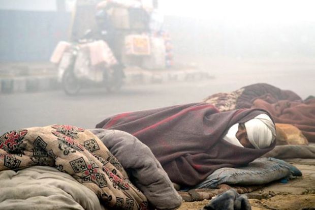 A homeless man wrapped in a blanket sleeps on the pavement on a cold winter day, in Gurugram, Saturday. (PTI Photo) 