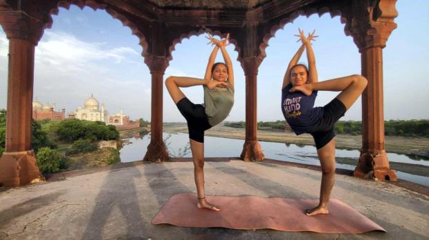 Young women perform yoga poses in the backdrop of the Taj Mahal, a day before International Day of Yoga, in Agra. (PTI)