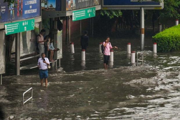 New Delhi: People wait at a waterlogged bus stop after heavy rainfall. (PTI)