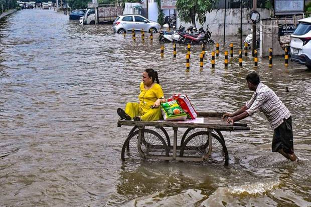 A labourer pushes a cart carrying a woman to assist her cross a flooded road in Vadodara. (Photo source: PTI)