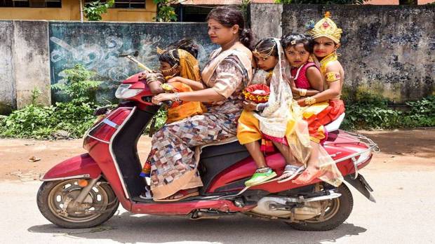 A woman riding a two-wheeler with children decked up as Lord Krishna and Goddess Radha on the occasion of the Janmashtami festival, in Chikkamagaluru. (Photo source: PTI)