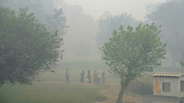 Labourers walk through a park amid low visibility caused by smog as air quality remains poor. (PTI)