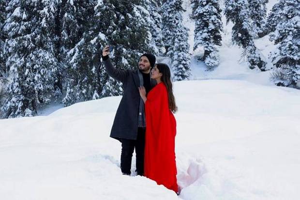 A tourist couple takes a selfie in a snow-covered field in Gulmarg. (Photo source: Reuters)