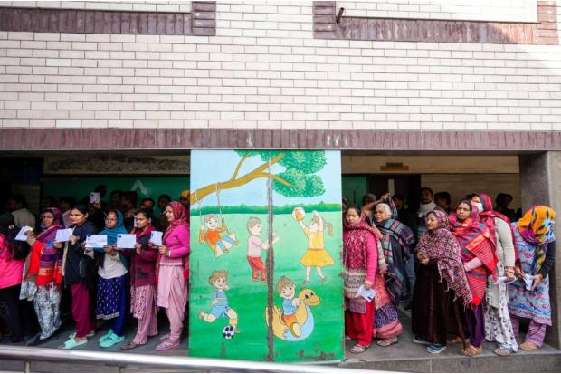 Voters wait in a queue at a polling booth to cast votes during the Delhi Assembly elections, at Trilokpuri.