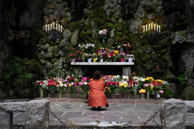A woman prays after placing flowers at The Grotto Cave and Outdoor Altar on Monday, April 21, 2025, in Portland, Ore.