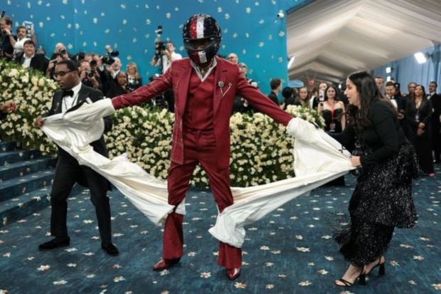 The Met Gala red-carpet is incomplete without some iconic outfit reveals. Damson Idris nailed the element of surprise as he turned up in a bedazzled helmet and white suit. Ripped in two pieces, he revealed a Tommy Hilfiger race suit. (Image: Reuters)