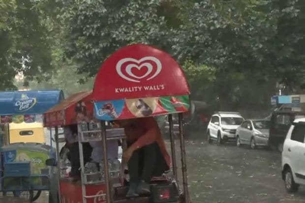 A difficult situation for hawkers and street vendors, ice-cream sellers were seen taking shelter under their own cart to protect themselves from the torrential rains in Delhi NCR. (Image: ANI)