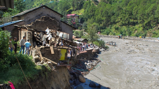 People gather near a house after it was partially washed away by the Beas river flowing in spate due to heavy rainfall, in Kullu district, Himachal Pradesh. (Photo Source: PTI)