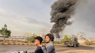 People ride a motorbike as smoke billows following Israeli airstrikes on multiple areas including a power planet and a gas station in Sanaa (Photo: AP)