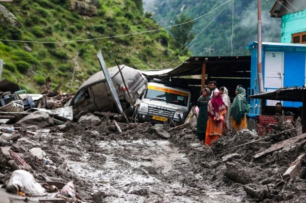Locals stand near damaged vehicles and debris following a cloudburst in Kishtwar district, Jammu and Kashmir. (Image source: PTI)