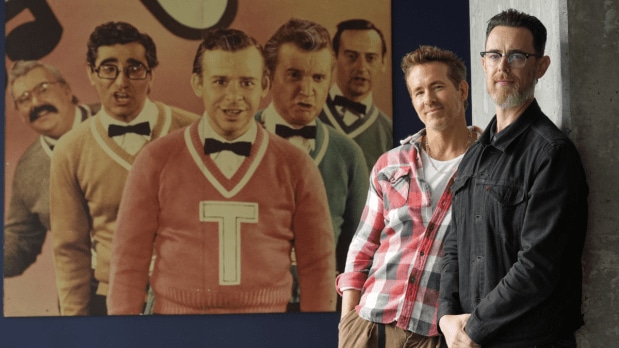 Colin Hanks (right), director, poses confidently with producer Ryan Reynolds (left) before a Second City cast photo, honoring comedy legend John Candy at TIFF.