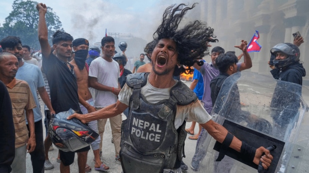 A protester wearing flak jacket and carrying a shield snatched from a policeman shouts slogans at the Singha Durbar, the seat of Nepal's government's various ministries and offices. (Photo Source: Associated Press)