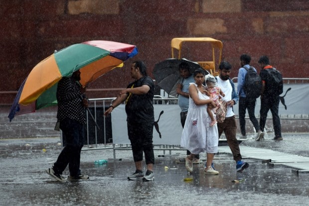 Visitors shield themselves with umbrellas while making their way around the Red Fort as heavy rain pours down, turning the historic monument into a striking sight against the gloomy weather. (Source: ANI)