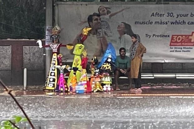 Heavy rain in Delhi leaves Ravana effigies damaged as people take shelter at a bus stop, waiting for the showers to subside. (Express Photo)
