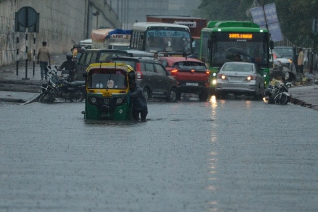 Commuters carefully navigate through a waterlogged stretch of road as heavy rainfall continues to cause disruption and slow movement across the city. (Source: PTI)