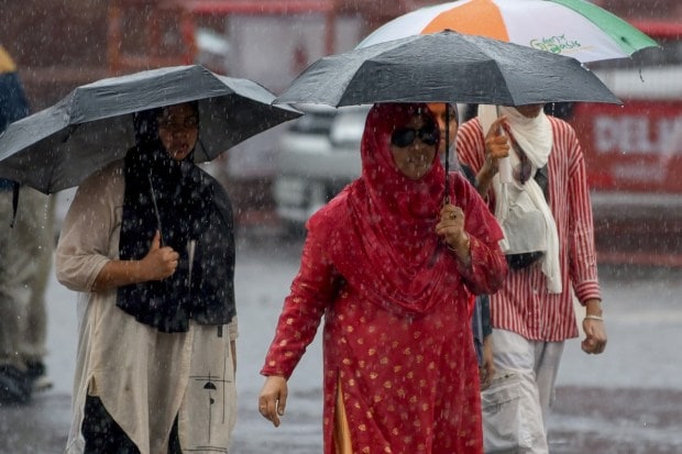 Visitors huddle under umbrellas to shield themselves from the downpour while exploring the historic Red Fort, as the rain adds a dramatic backdrop to the monument. (Image: ANI)