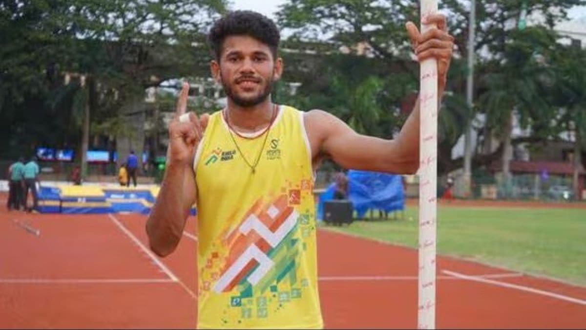 Indian pole vaulter Dev Kumar Meena and his coach Ghanshyam standing with long fiberglass poles at a railway station. The image illustrates the logistical challenges of transporting high-value, fragile athletic equipment on Indian Railways.