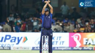 An IPL umpire standing on the field with arms crossed above his head in an 'X' shape to signal the introduction of an Impact Player.