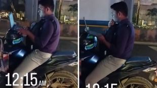 Man sitting on a parked motorcycle at night in Bengaluru working on a laptop, with the screen illuminating his face in the dark.