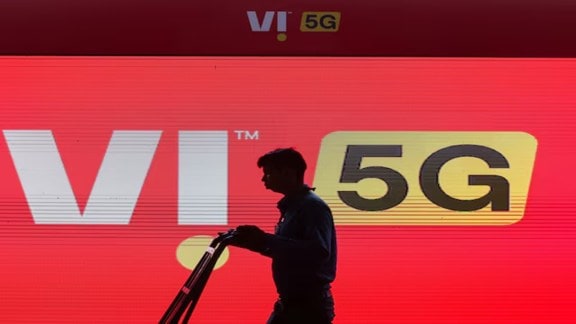 Vodafone Idea mobile network tower reflecting against a smartphone screen showing financial stock market graphs.