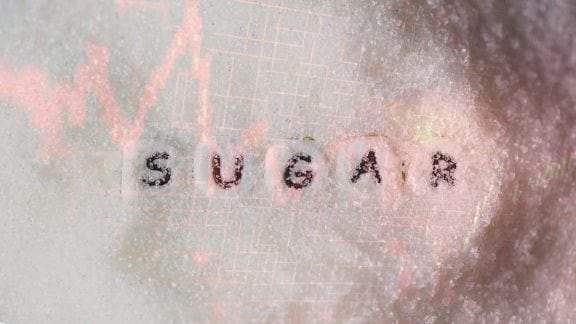 A visual showing a pile of refined sugar in the foreground with a "Prohibited" stamp overlay and a blurred background of a sugar mill, symbolizing the current policy shift and supply constraints.