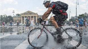 A cyclist rides in front of a police water cannon hose spraying a cooling mist in Budapest AP