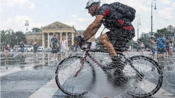 A cyclist rides in front of a police water cannon hose spraying a cooling mist in Budapest AP